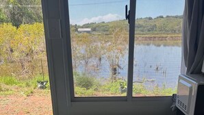 Une pièce dotée d’une grande fenêtre donnant sur un plan d’eau et sur la verdure. On y trouve un bureau avec un ordinateur et une chaise.
