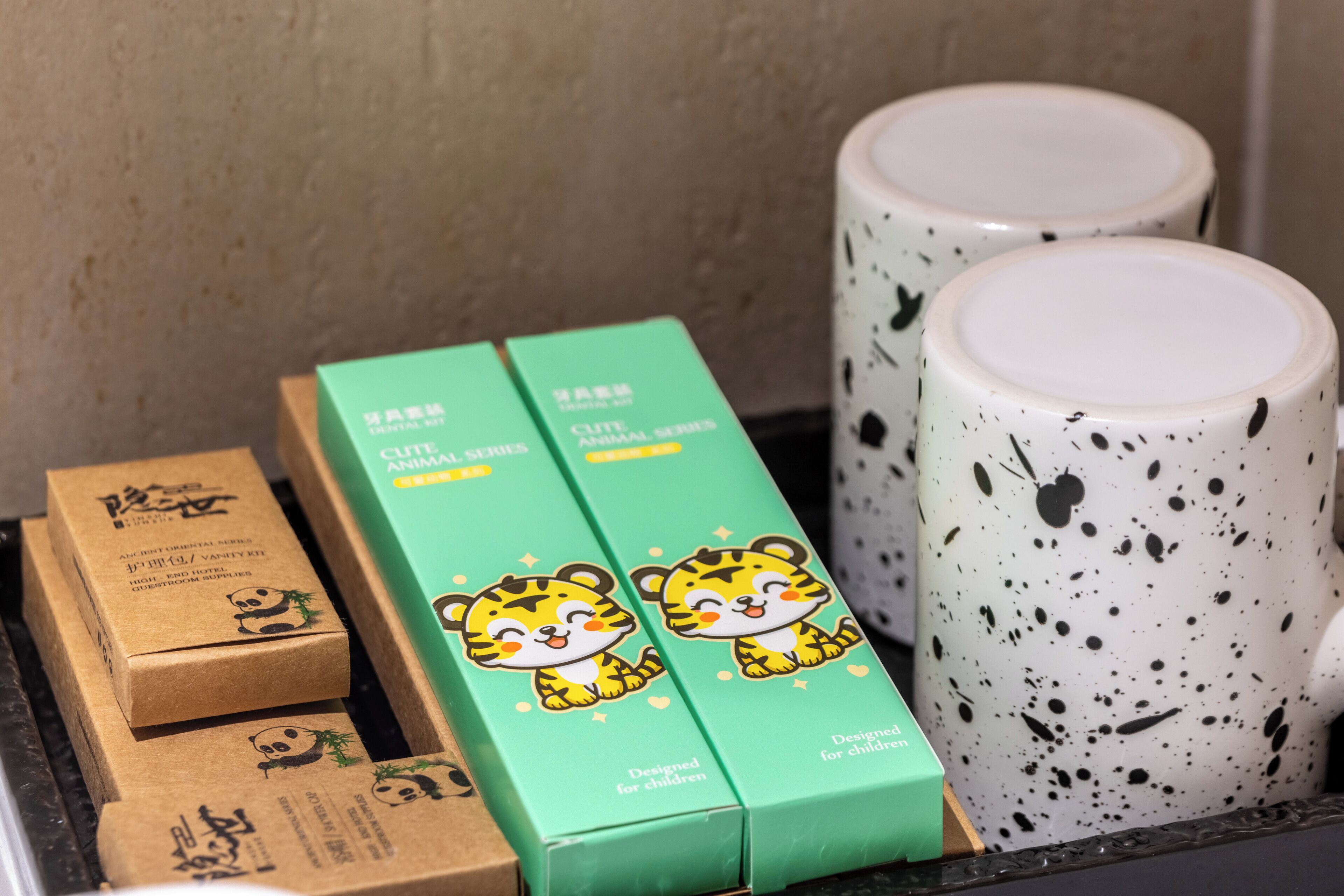 A set of green boxes with cartoon tiger designs, a white mug with black speckles, and a brown box with panda illustrations.