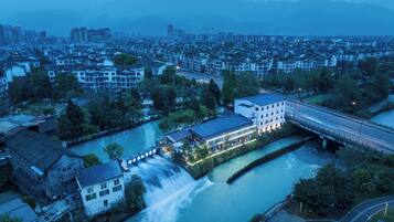 An aerial view of a riverside town with a prominent building featuring a large glass facade and a waterfall.