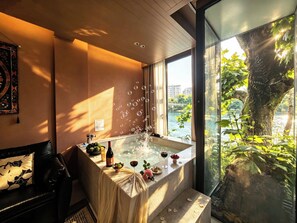 A room with a bathtub, a table with drinks, and a view of a tree and water outside. - Dujiangyan Private Hot Spring Villa (Chengdu)