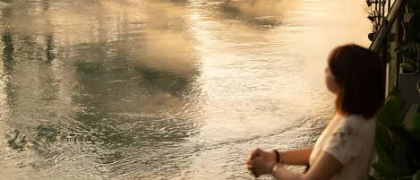 A person standing by a calm body of water, possibly a river or lake, with a railing on the right side.