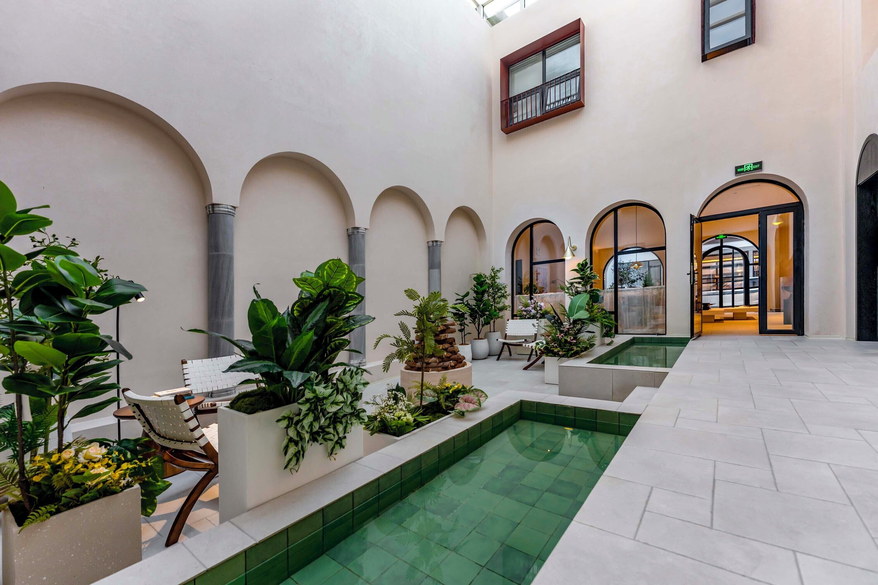 Un vaste patio intérieur avec une piscine centrale, entouré de jardinières contenant différentes plantes et agrémenté d’espaces pour s’asseoir.