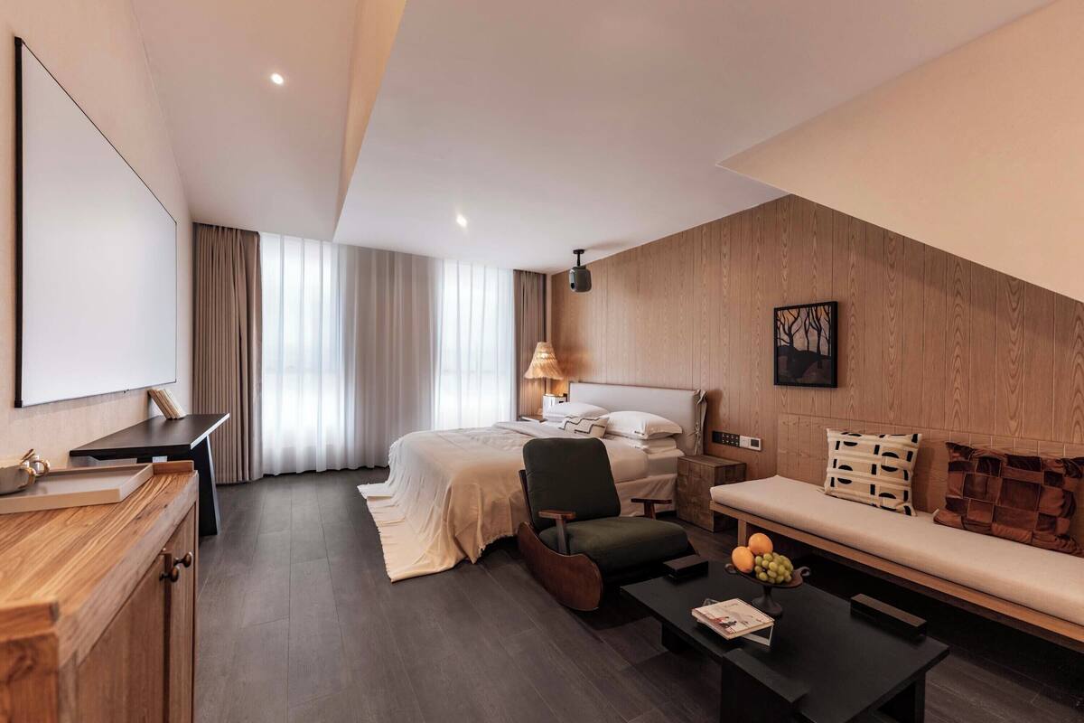 A modern hotel room with a bed, a desk, a chair, a sofa, and a coffee table.