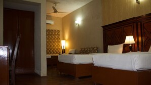 A hotel room with two beds, a wooden headboard, a desk, a chair, a ceiling fan, and a patterned wallpaper.