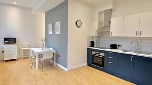 A modern kitchen with white cabinets, a built-in oven, and a dining area with a white table and chairs. - Shoreditch Apartments by PrimeCityHosts F4 (Greater London)