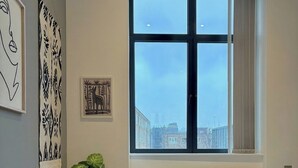 A bedroom with a bed, a window with a view, a radiator, and wall art. - Shoreditch Apartments by PrimeCityHosts F4 (Greater London)