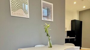 A dining area with a white table, four chairs, a vase with a plant, and two framed artworks on the wall. - Shoreditch Apartments by PrimeCityHosts F4 (Greater London)