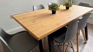 A modern dining area with a wooden table, grey chairs, and two potted plants. - Shoreditch Apartments by PrimeCityHosts F5 (Greater London)