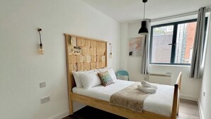A single bed with a wooden headboard, white bedding, and a window with a view of buildings. - Shoreditch Apartments by PrimeCityHosts F5 (Greater London)