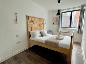 Ein Einzelbett mit Holz-Kopfteil, weißer Bettwäsche und einem Fenster mit Blick auf Gebäude.