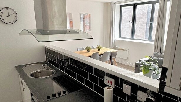 A modern kitchen with a black countertop, stainless steel sink, and a window with curtains. - Shoreditch Apartments by PrimeCityHosts F5 (Greater London)