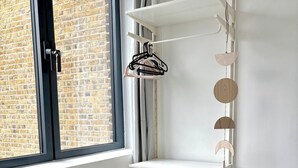 A corner room with a white chair, a multi-tiered white shelving unit, and a window with a view of a brick building. - Shoreditch Apartments by PrimeCityHosts F5 (Greater London)