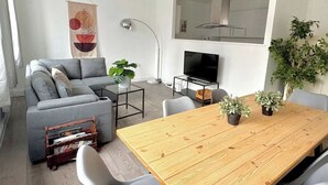 A modern living room with a grey sofa, a wooden dining table, and a TV stand. - Shoreditch Apartments by PrimeCityHosts F5 (Greater London)