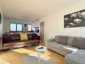A modern living room with a brown leather sofa, a grey sofa, and a small round table with remotes. - Shoreditch Apartments by PrimeCityHosts F7 (Greater London)