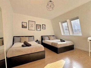A bedroom with two beds, a geometric light fixture, and a window with a view. - Shoreditch Apartments by PrimeCityHosts F7 (Greater London)