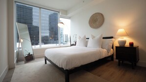 A bedroom with a large window, a bed, a nightstand, and a mirror.