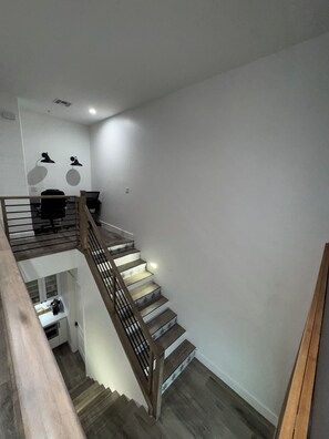 Eine moderne Treppe mit Holzhäckern und Metallgeländern, die zu einem Bereich im zweiten Obergeschoss mit Schreibtisch und Stuhl führt.