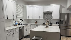 A modern kitchen with white cabinetry, a central island, stainless steel appliances, and a patterned backsplash. - Modern Luxury Townhouse –  3-Suite Retreat (Mesa)