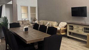 A modern living room with a dining area, a sofa set, a TV, and a wooden cabinet. - Modern Luxury Townhouse  –  3-Suite Retreat (Mesa)