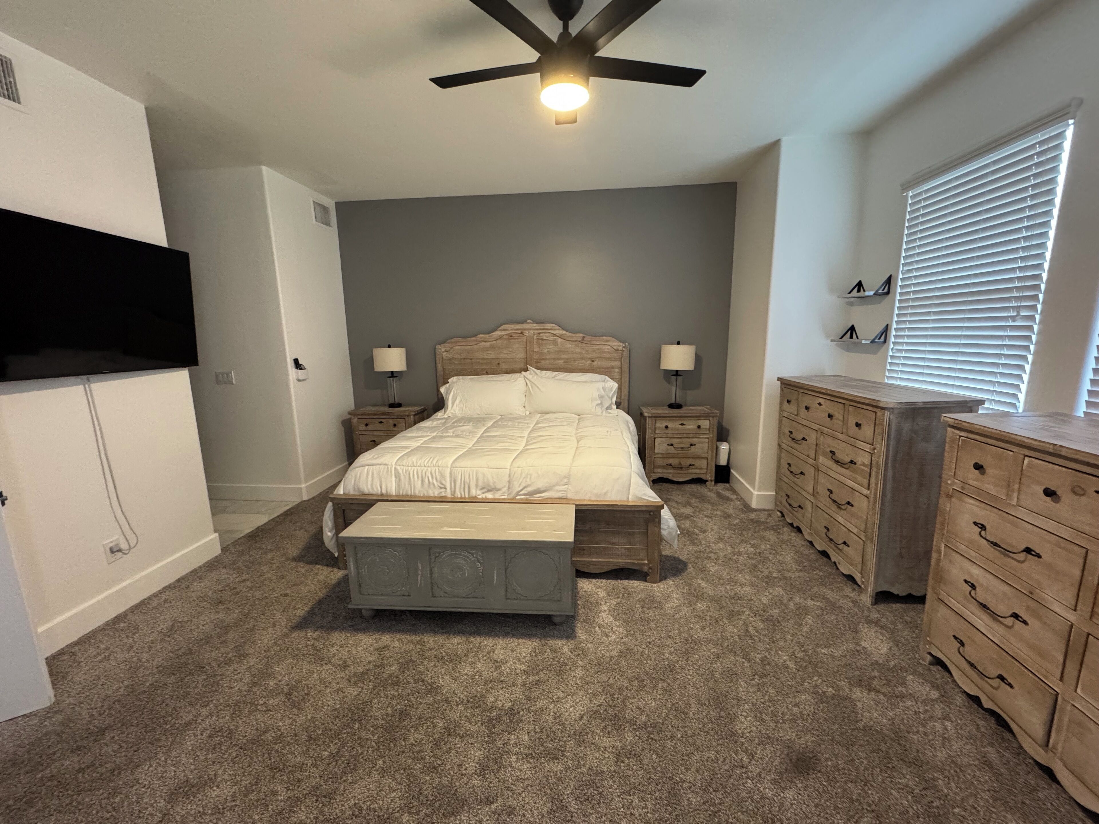 A bedroom with a bed, nightstands, a dresser, a ceiling fan, and a TV mounted on the wall.