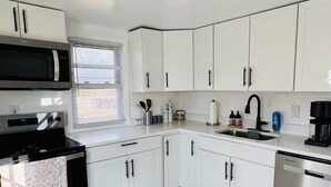 Una cocina moderna con armarios blancos, electrodomésticos de acero inoxidable y piso de mármol.