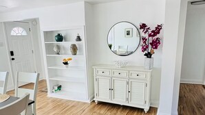 Una habitación moderna, bien iluminada, con comedor, armarios blancos y piso de madera.
