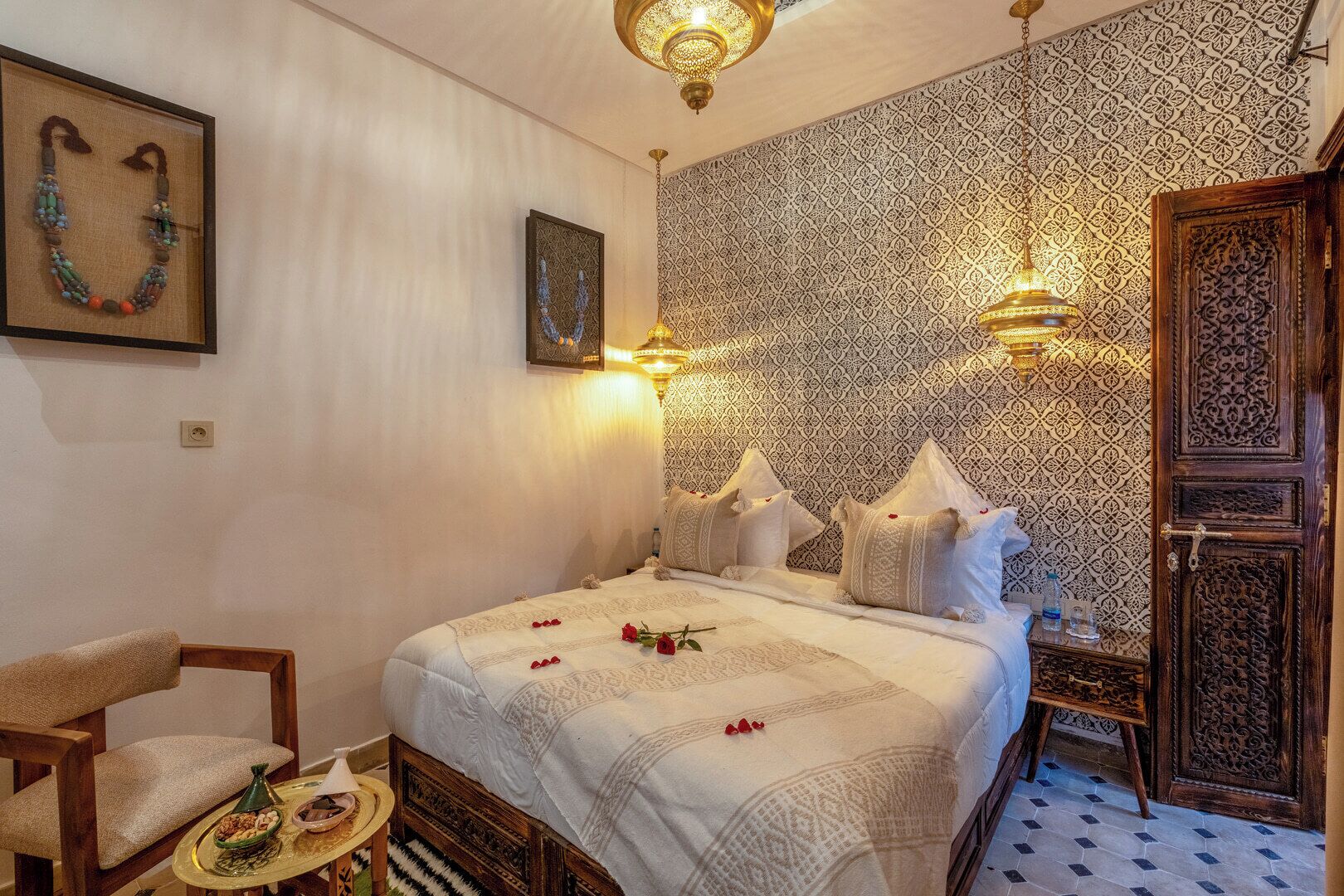 A traditional Moroccan room with a bed, a wooden chair, a decorative wall, and a patterned floor.