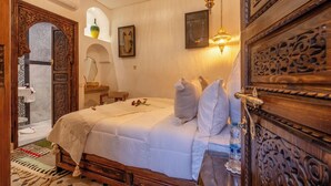 A traditional Moroccan-style bedroom with a wooden bed, ornate door, and decorative ceiling lights. - Elegant Riad Musée: Authentic Marrakech Charm in the Medina (marrakech)