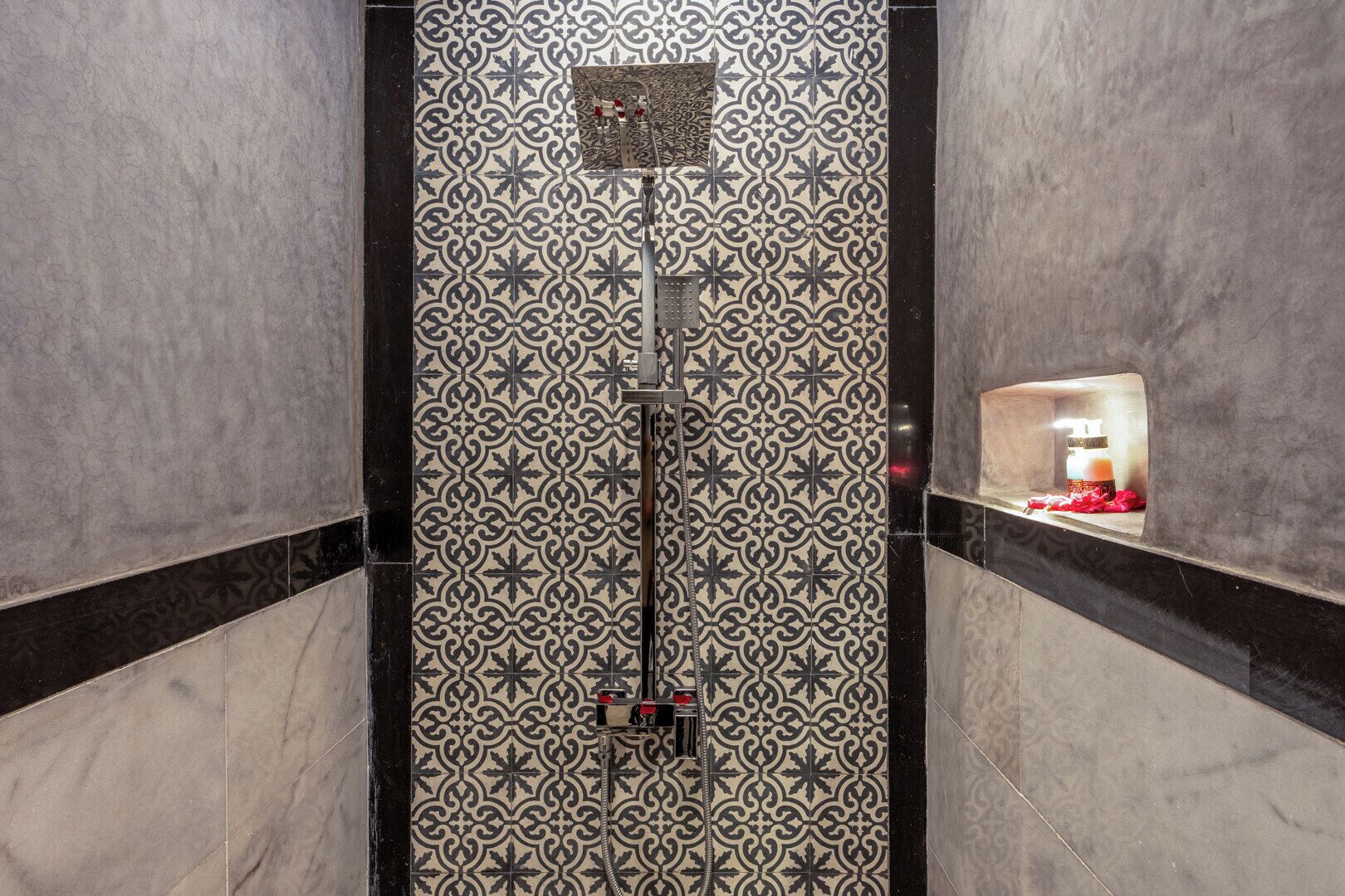 Un bagno con piastrelle decorate, una doccia e un piccolo ripiano con articoli da toilette.
