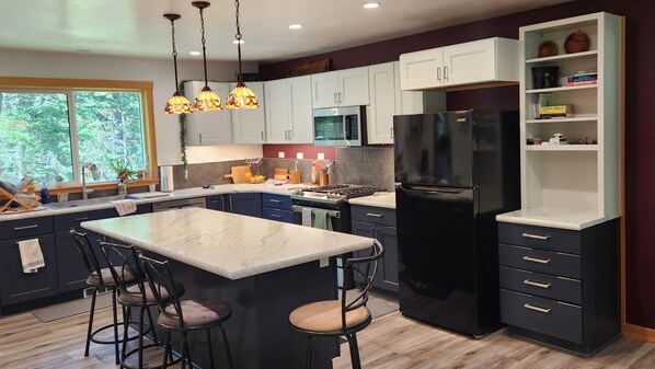 Una cocina moderna con una isla central, taburetes de bar, un refrigerador negro y armarios blancos.