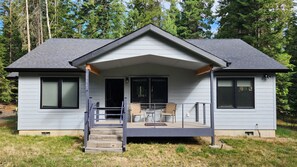 A two-story house with a covered porch, a front door, and a small outdoor seating area.