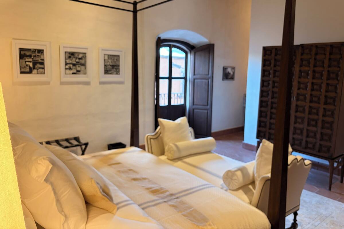 A bedroom with a bed, a chair, and a door. There are three framed pictures on the wall.