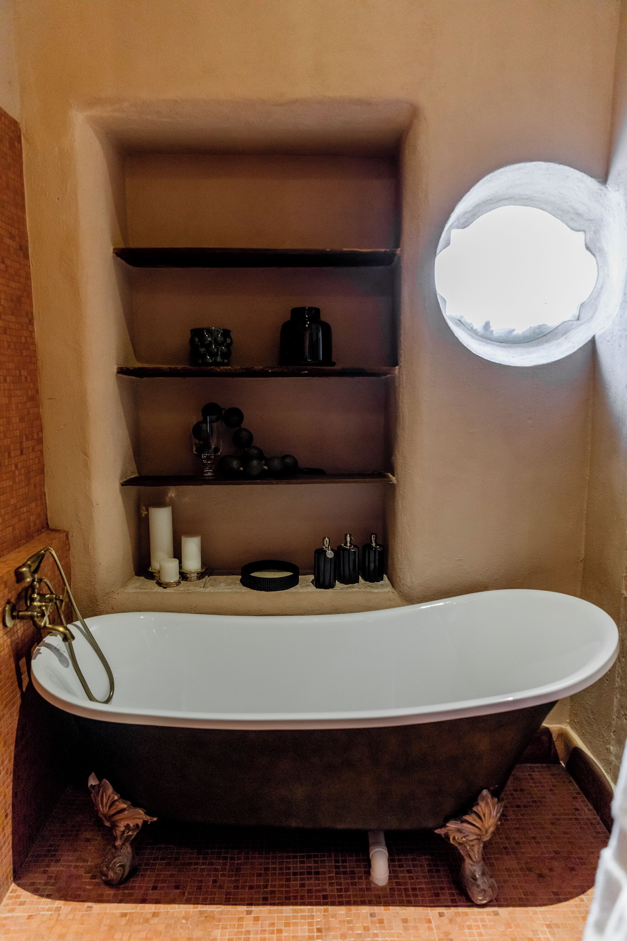 Un baño con una bañera independiente, repisas con artículos de aseo y un ventanal.