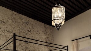 Una cama con dosel, un sofá tapizado en color crema, suelo de madera y pared de piedra texturizada.