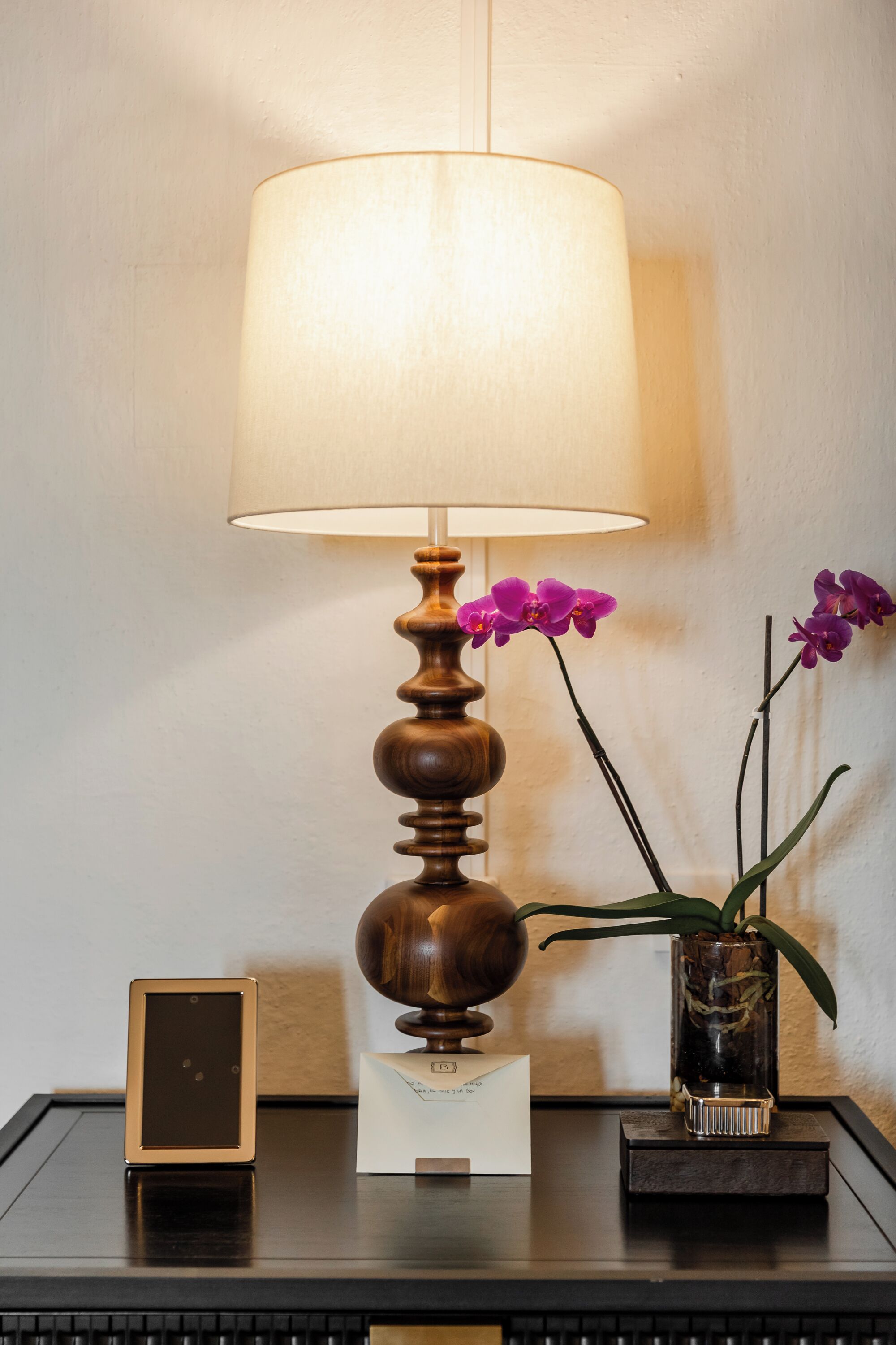 Uma mesa com uma luminária, uma fotografia emoldurada e um vaso com orquídeas.