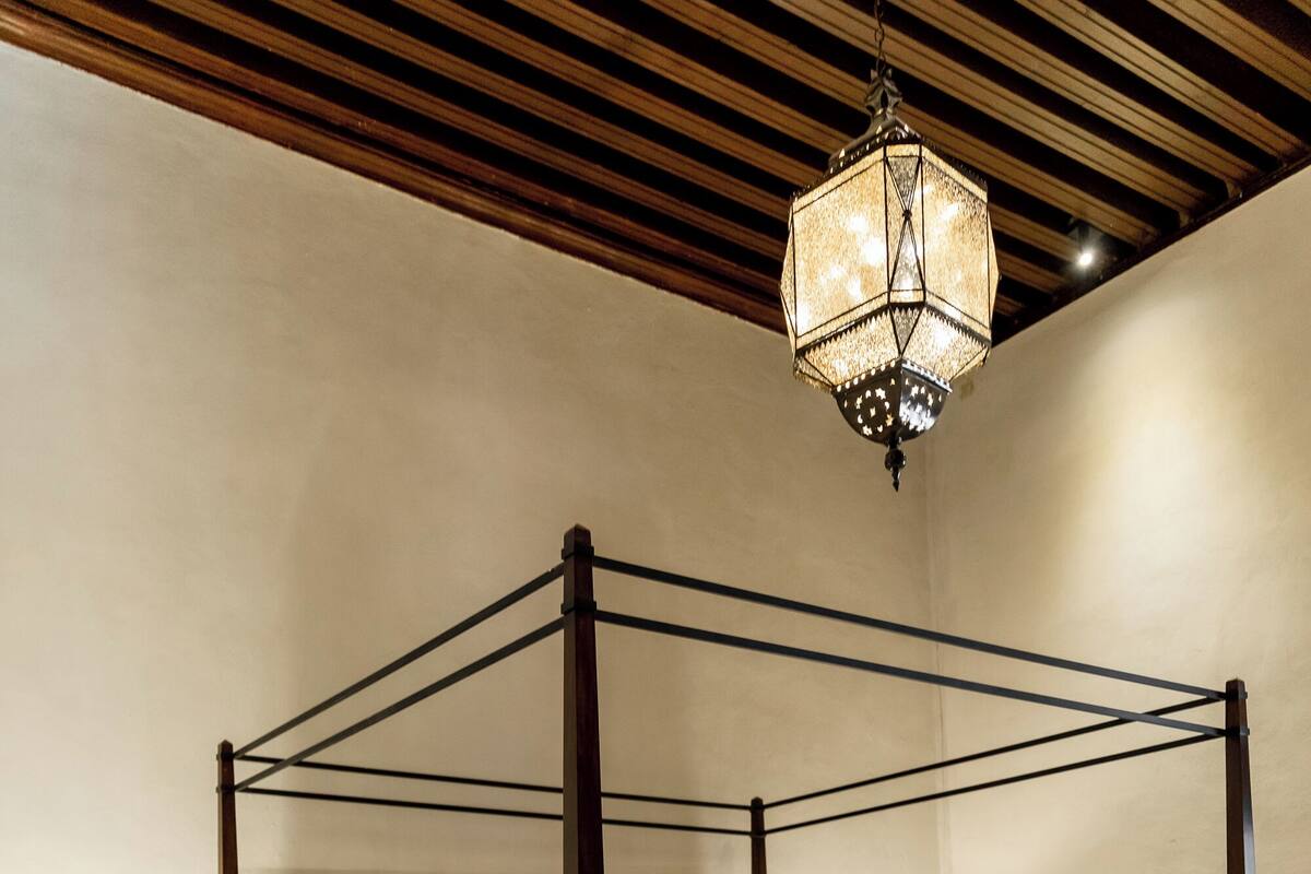 A four-poster bed with a canopy, bedside tables, a bench, and a hanging light fixture in a hotel room.