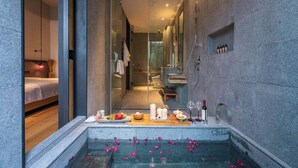 A modern bathroom with a glass-enclosed shower, a bathtub with rose petals, and a wooden vanity. - Tan She Tang Quan Resort Hotel-Huangshan (Huangshan)
