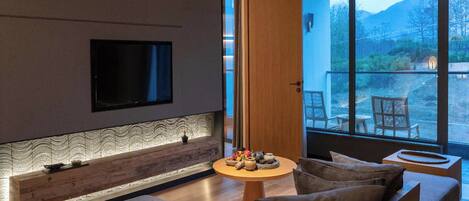 A modern living room with a flat-screen TV mounted on the wall, a wooden accent wall, a round coffee table with decorative items, and a sofa with cushions.