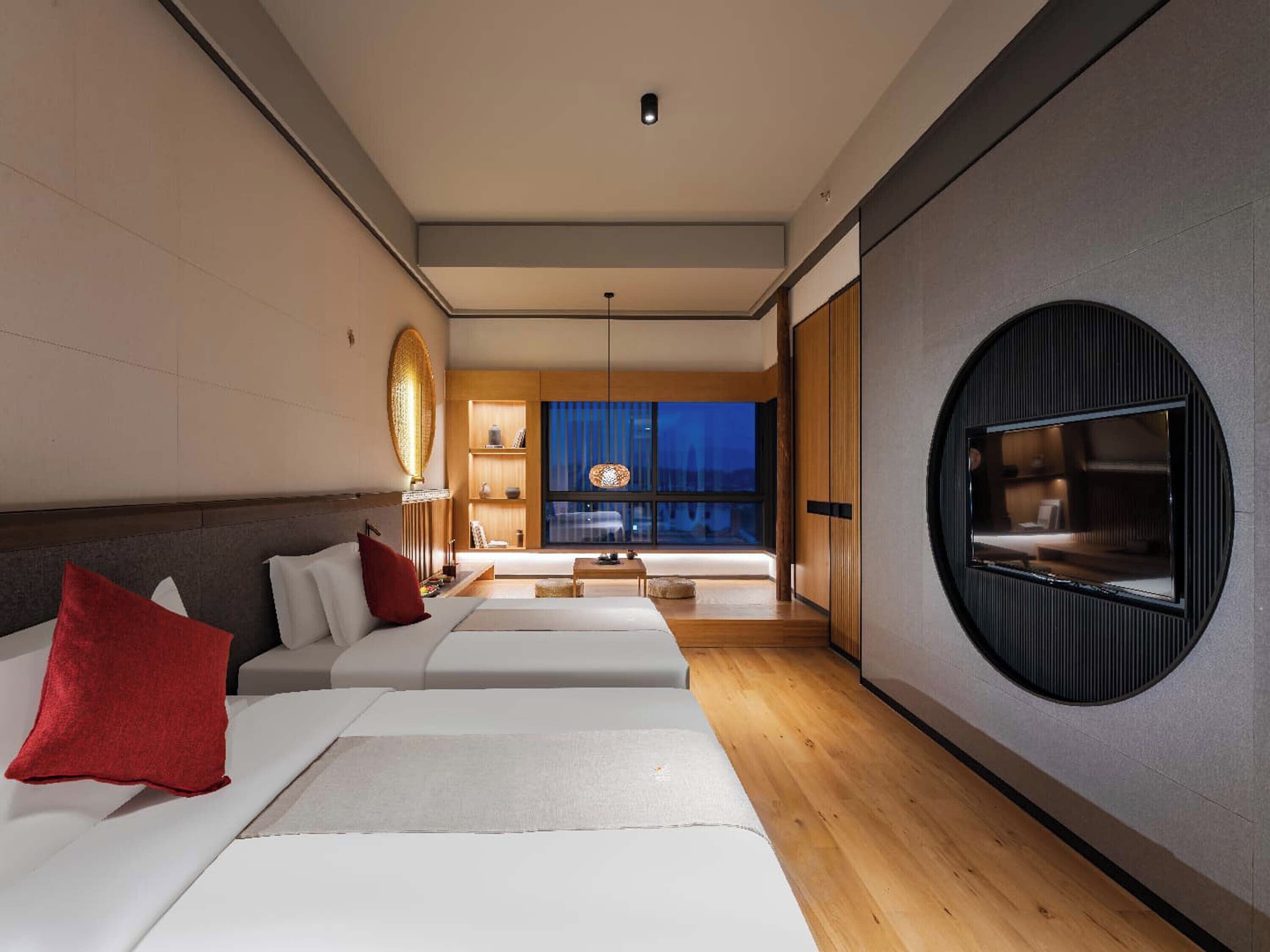 A modern hotel room with a large bed, a smaller bed, a TV, and a view of the city at night.