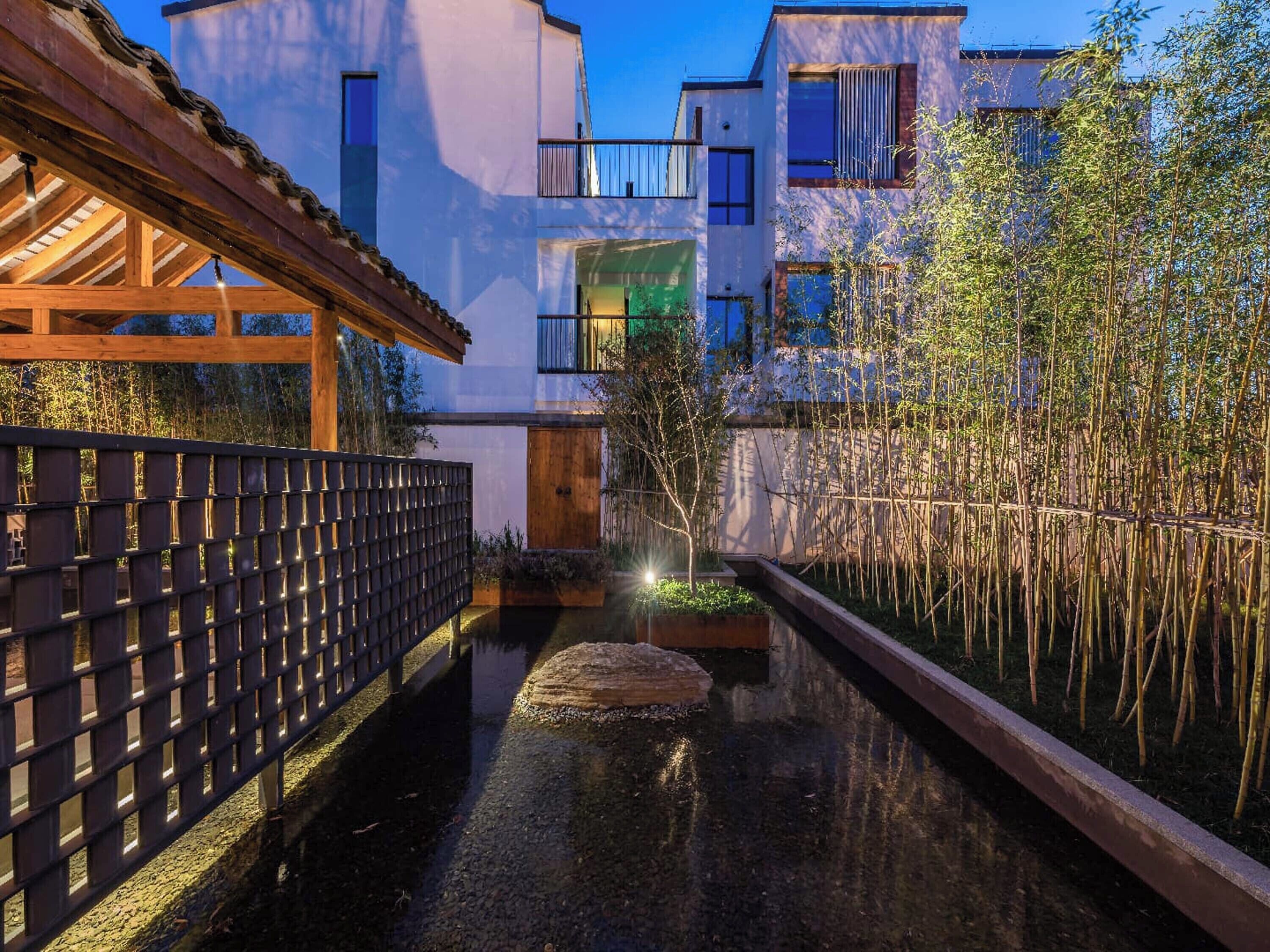 A modern building with a wooden deck, a narrow water channel, and bamboo plants.