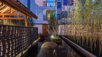 A modern building with a wooden deck, a narrow water channel, and bamboo plants.