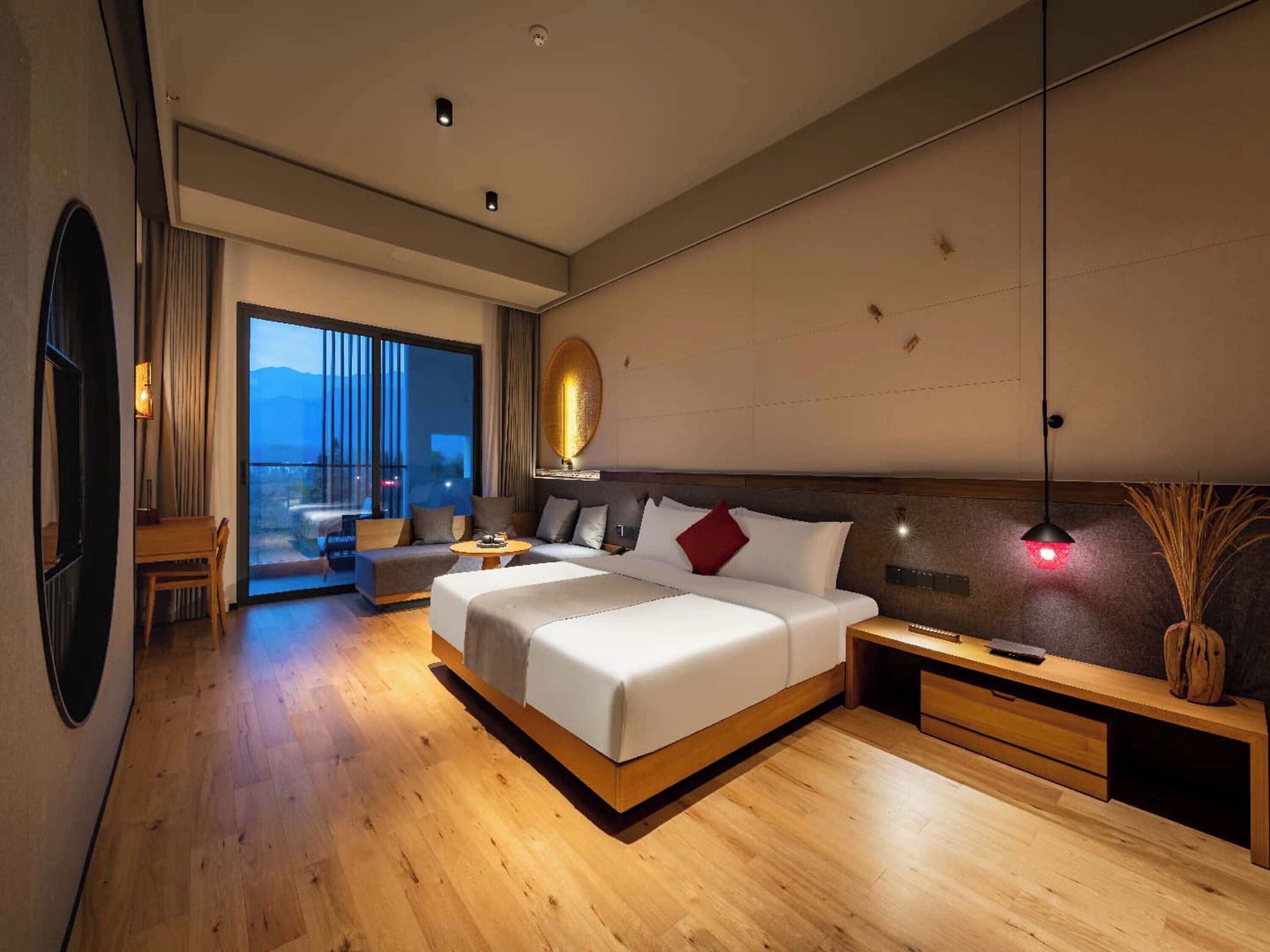 A modern hotel room with a large bed, a seating area, and a view of the mountains.
