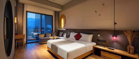 A modern hotel room with a large bed, a seating area, and a view of the mountains.