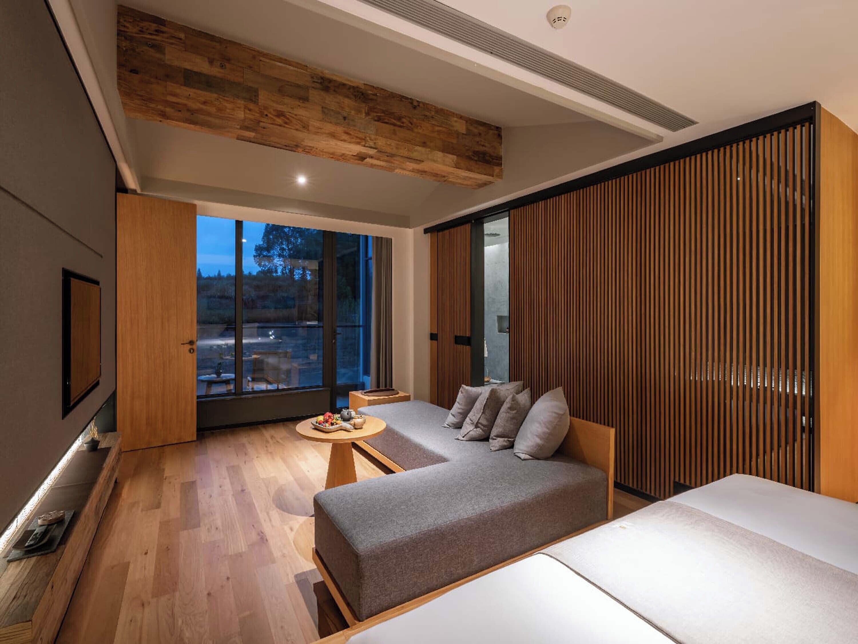 A modern bedroom with a sofa, a small table, and a large window.