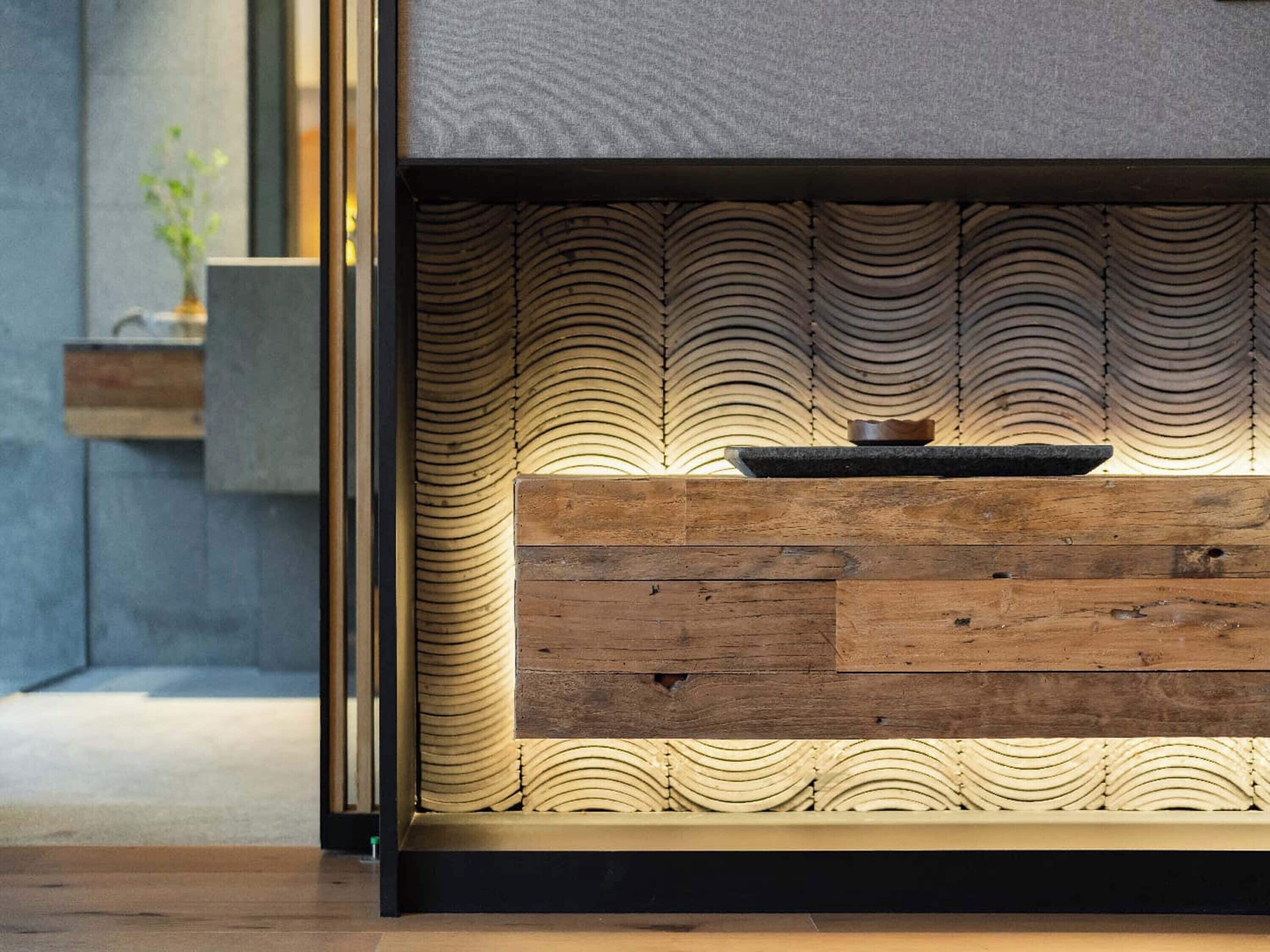 A modern interior with a wooden bench, a textured wall, and a small table with a bowl.