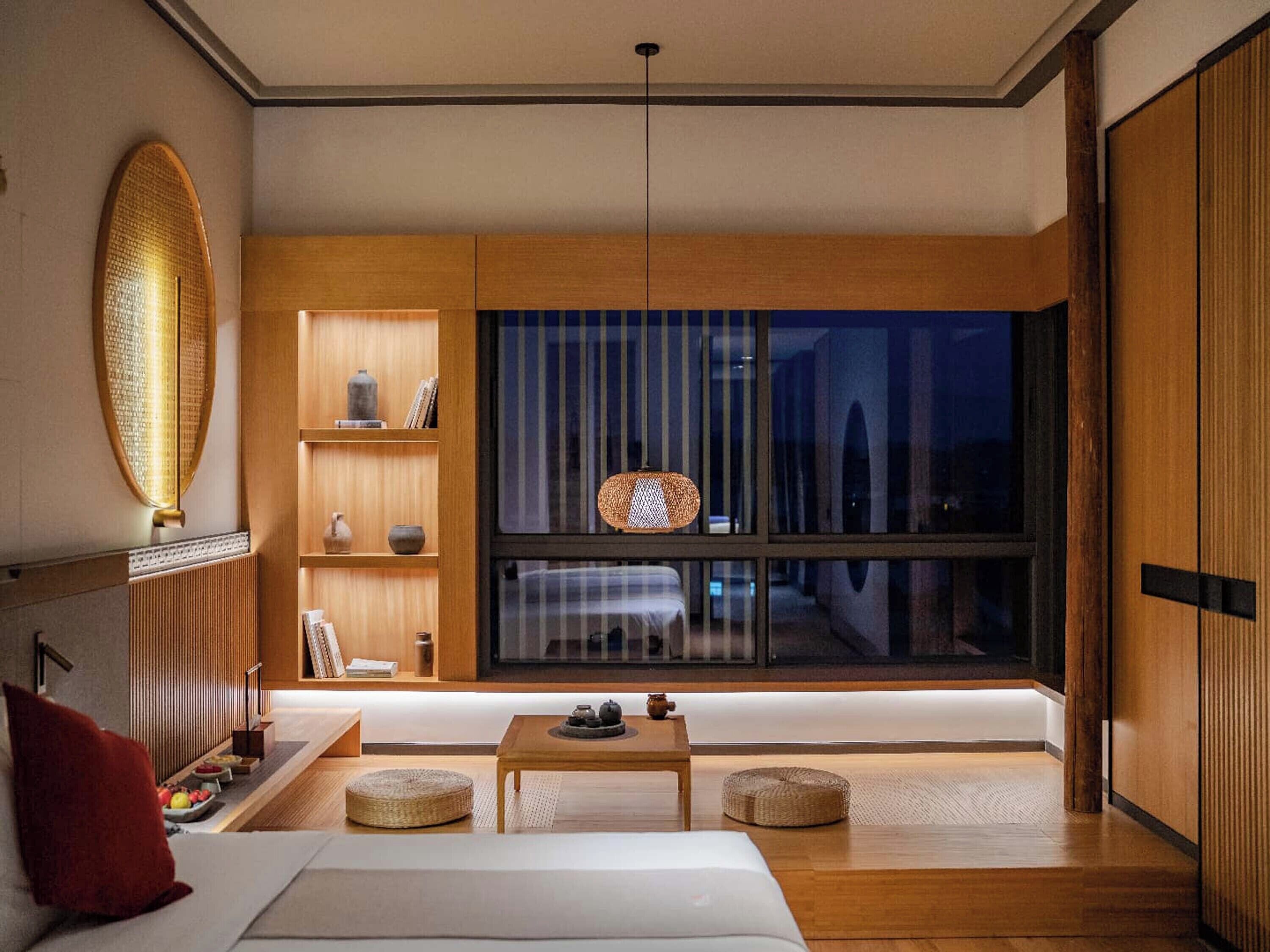 Ein modernes Hotelzimmer mit großem Fenster, Holzmöbeln und einer Hängeleuchte.