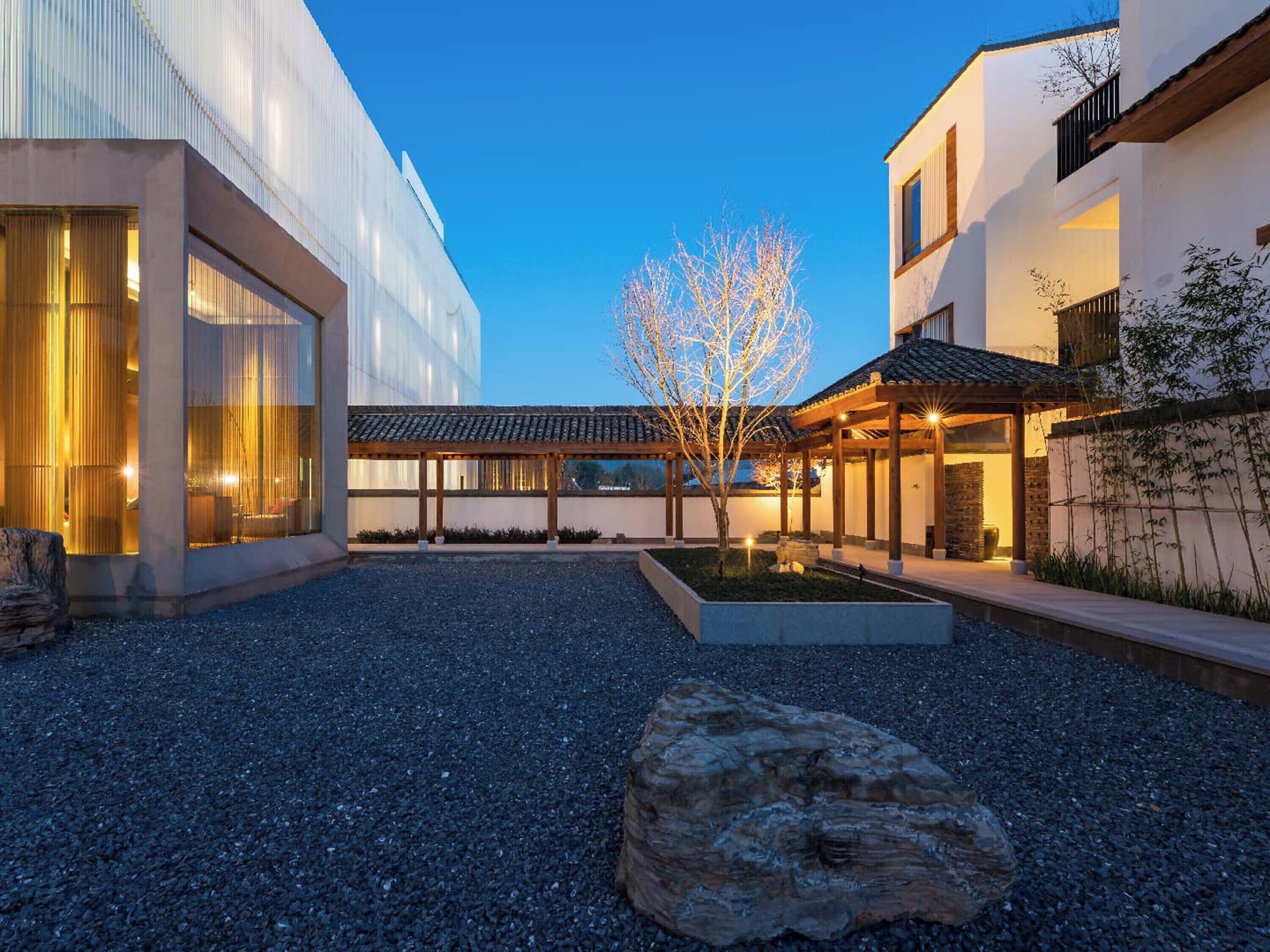 Un edificio moderno con patio, ventanas grandes y un árbol.