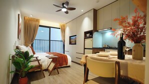 A modern hotel room with a bed, a dining table, a chair, a potted plant, a ceiling fan, and a view of the outside balcony.