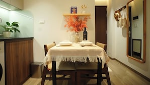 A dining area with a table set for two, a potted plant, a decorative vase, and a book on a shelf above the table.