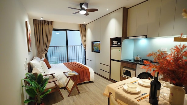 A hotel room with a bed, a dining table set for two, a kitchen area, and a balcony with a view.